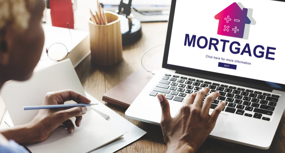 A woman typing on a laptop with a screen that says “mortgage”.