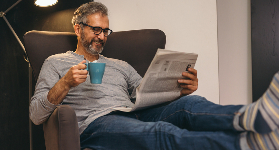 A man drinking a coffee at home with his feet up.