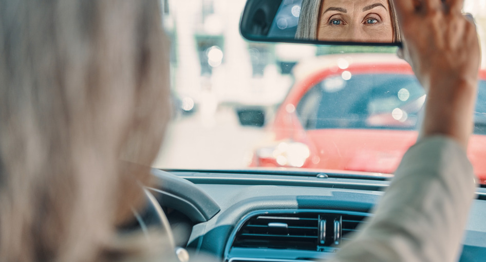 A driver adjusting the rear view mirror in a car.